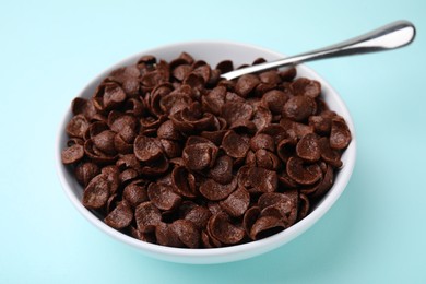 Photo of Breakfast cereal. Chocolate corn flakes in bowl and spoon on light blue table, closeup