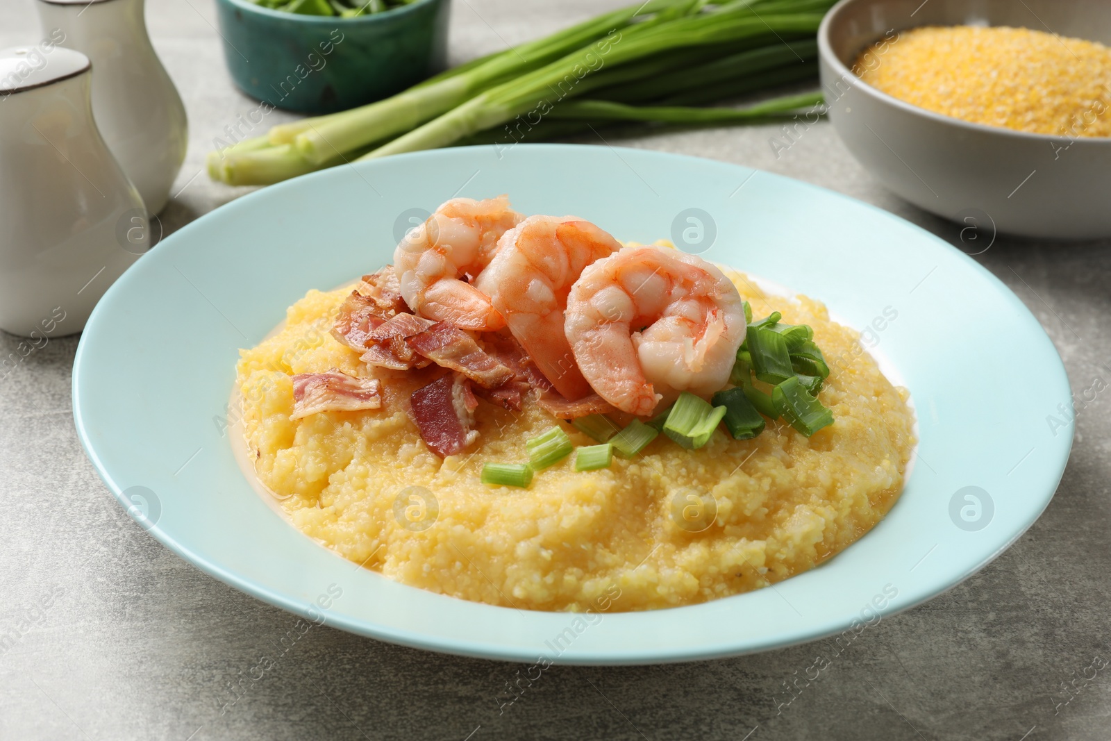 Photo of Plate with fresh tasty shrimps, bacon, grits and green onion on grey table