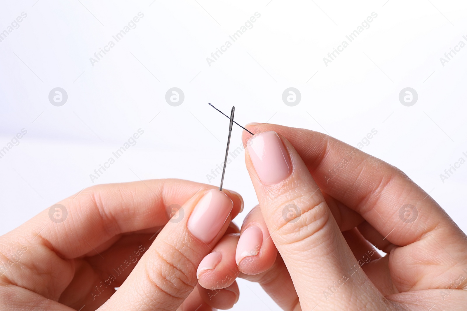 Photo of Woman threading sewing needle on white background, closeup