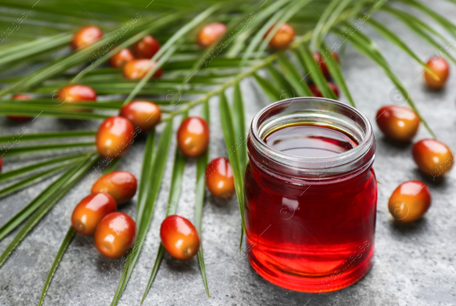 Photo of Palm oil in glass jar, tropical leaves and fruits on grey table