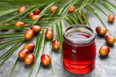 Palm oil in glass jar, tropical leaves and fruits on grey table