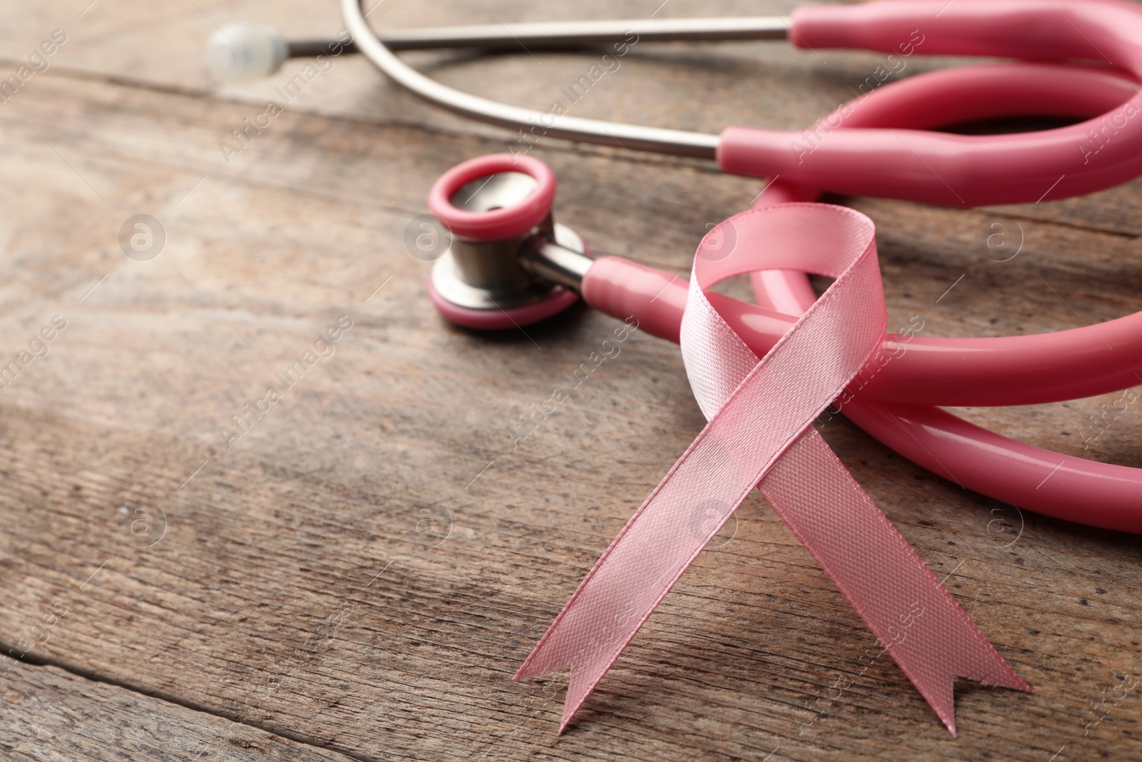 Photo of Pink ribbon and stethoscope on wooden background, space for text. Breast cancer concept