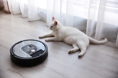 Photo of Modern robotic vacuum cleaner and cute cat on floor indoors