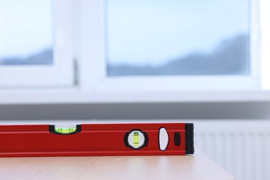 Photo of Red building level on wooden table indoors, closeup. Space for text