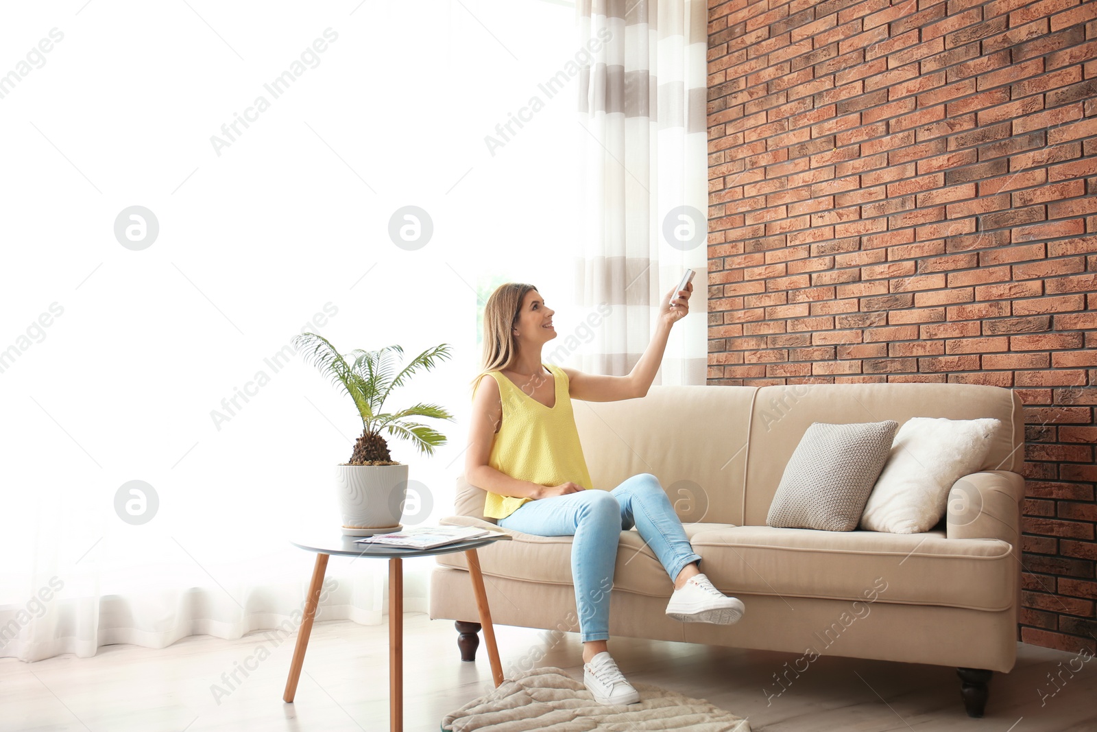 Photo of Woman with air conditioner remote at home