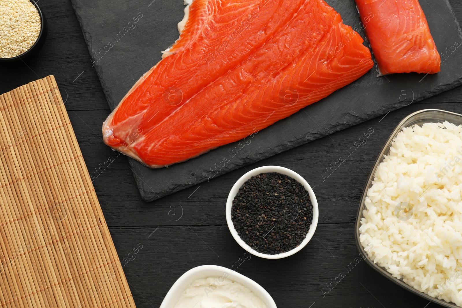 Photo of Making sushi rolls. Flat lay composition with fresh salmon and other ingredients on black wooden table