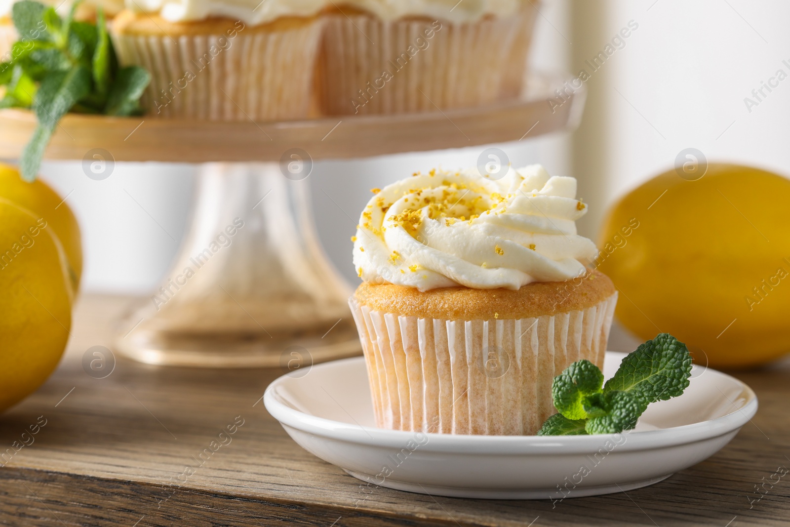 Photo of Delicious lemon cupcake with white cream and mint on wooden table, closeup