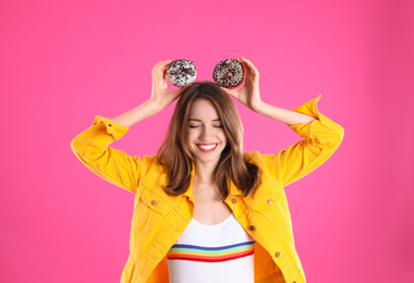 Beautiful young woman with donuts on pink background