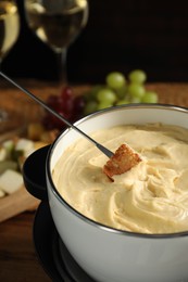 Photo of Dipping piece of bread into fondue pot with melted cheese at table, closeup