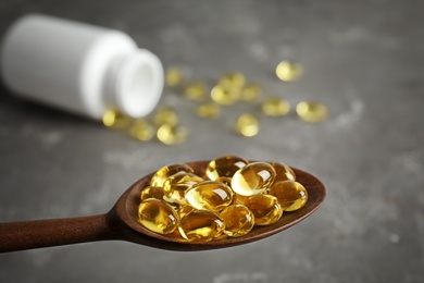 Photo of Spoon with cod liver oil pills over table, closeup