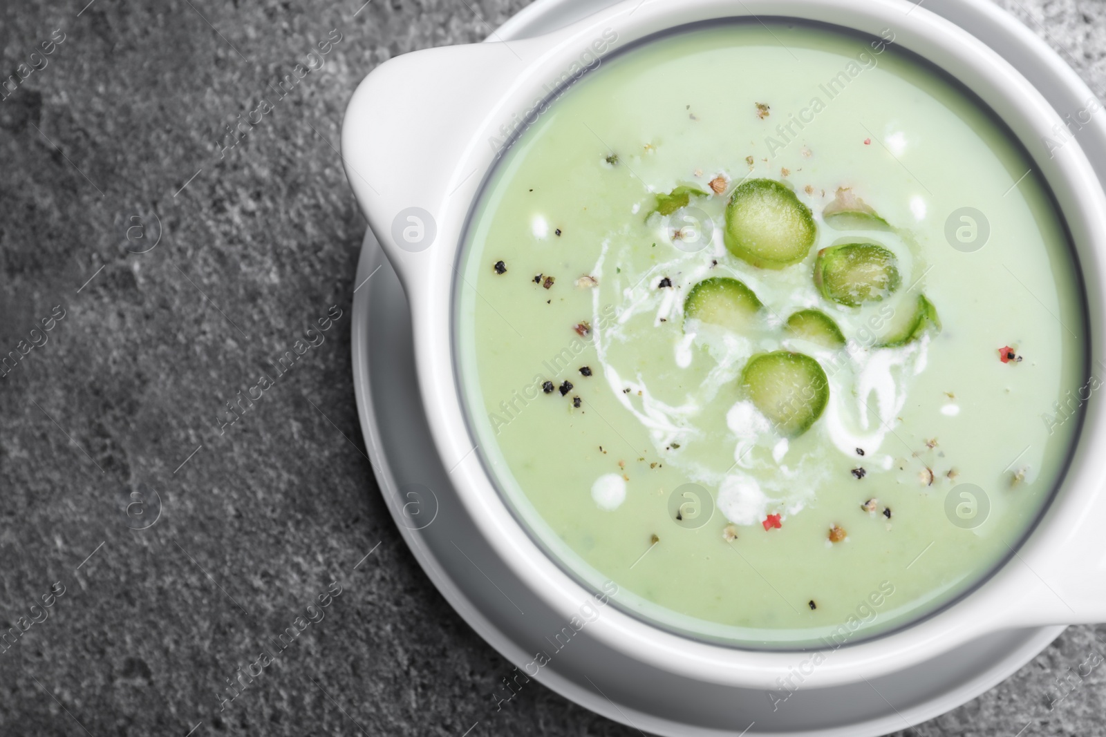 Photo of Bowl of delicious asparagus soup on grey table, top view. Space for text