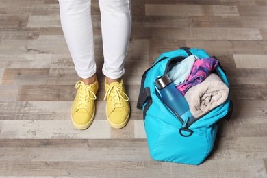 Photo of Young woman in sportswear and bag with gym equipment indoors