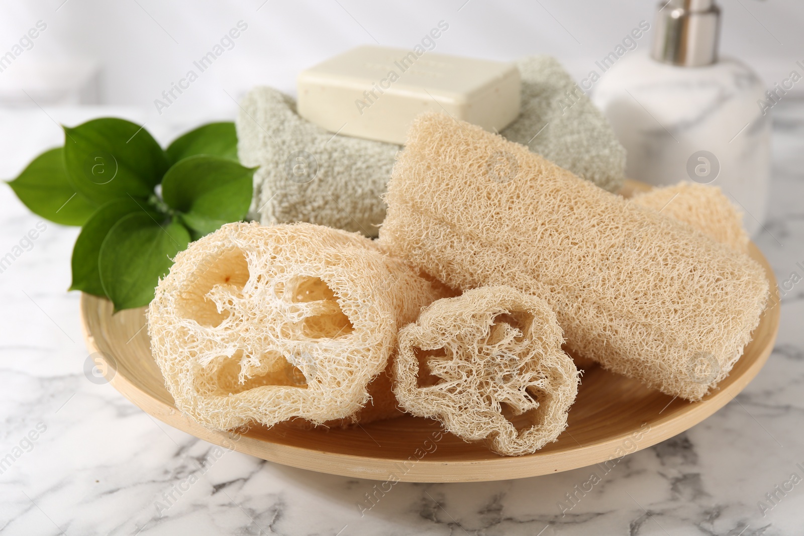 Photo of Loofah sponges, soap, towel and green leaves on white marble table