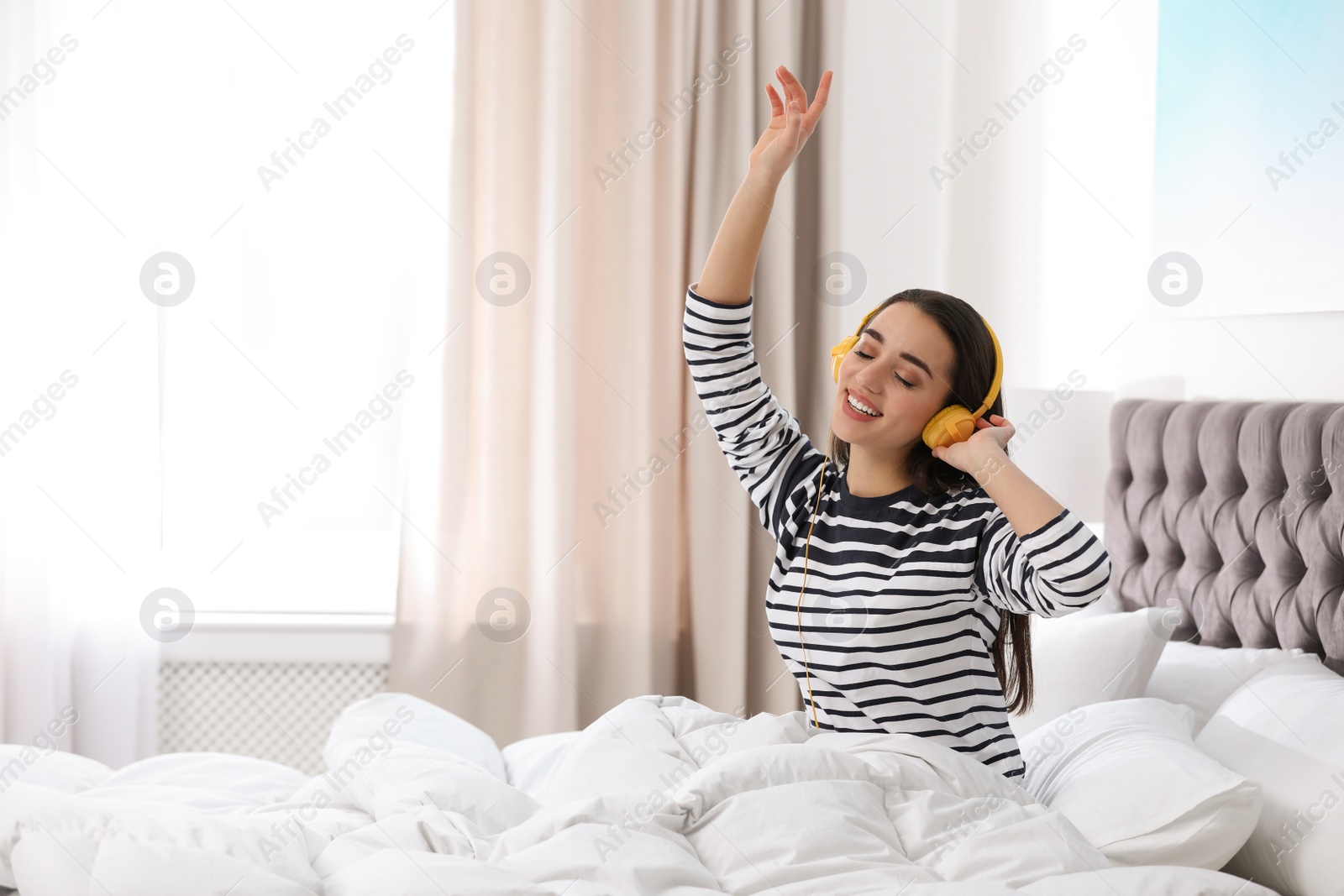 Photo of Young woman with headphones enjoying music in bed