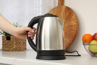 Photo of Woman with electric kettle in kitchen, closeup