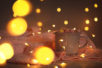 Cup of delicious hot cocoa with marshmallows and fairy lights, bokeh effect