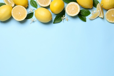 Many fresh ripe lemons with green leaves and flowers on light blue background, flat lay. Space for text