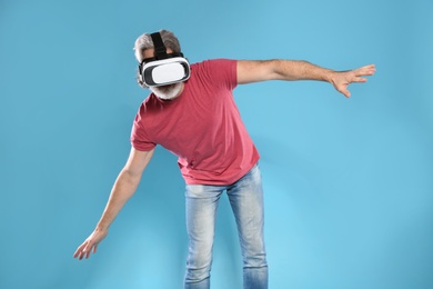 Emotional mature man playing video games with virtual reality headset on color background