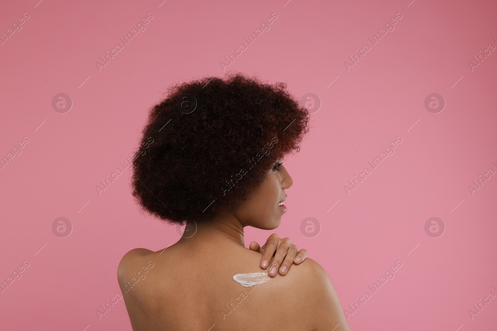 Photo of Beautiful young woman applying body cream onto back on pink background