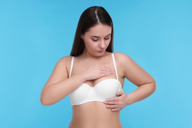 Photo of Mammology. Woman in bra doing breast self-examination on light blue background