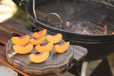 Photo of Slices of fresh peaches on wooden table near grill outdoors