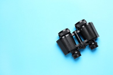 Photo of Modern binoculars on light blue background, top view. Space for text