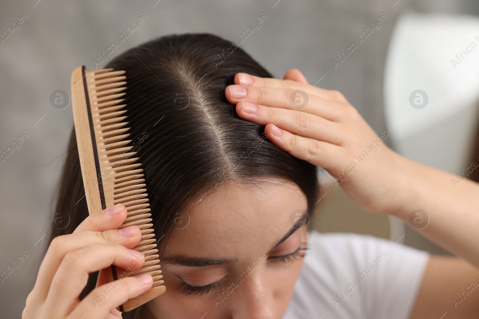 Photo of Woman with comb examining her hair and scalp on blurred background, closeup