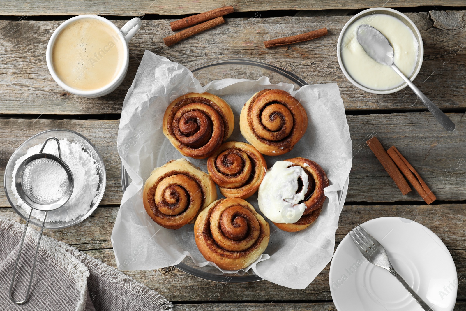 Photo of Tasty cinnamon rolls and ingredients on wooden table, flat lay