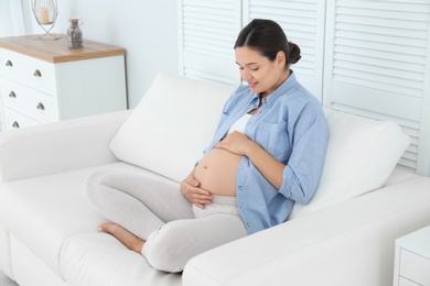 Beautiful pregnant woman sitting on sofa at home