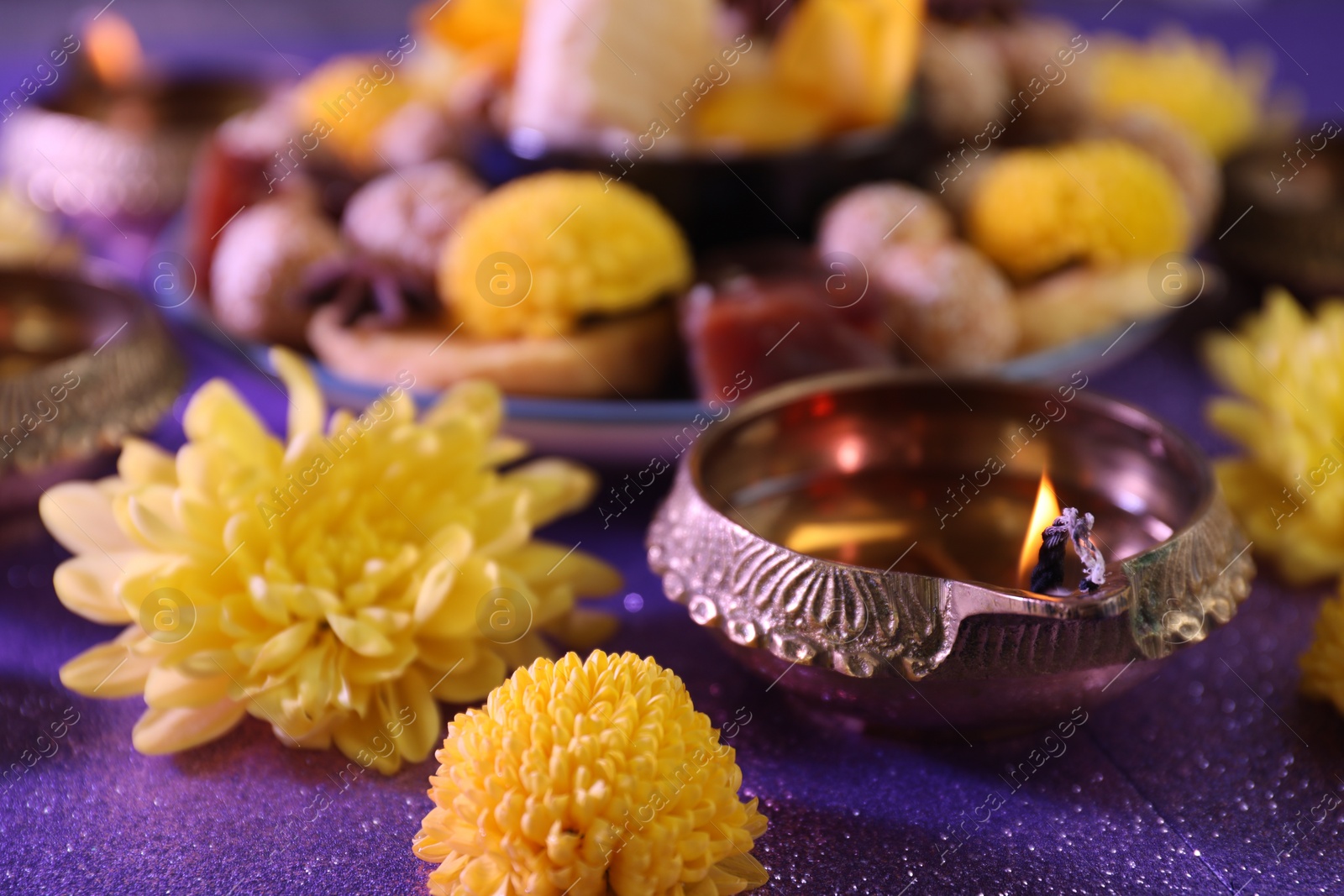 Photo of Diwali celebration. Diya lamp and chrysanthemum flowers on shiny violet table, closeup