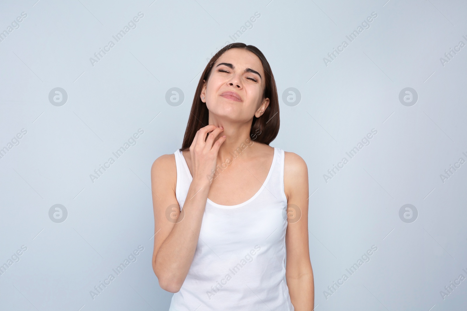 Photo of Young woman scratching neck on light background. Annoying itch