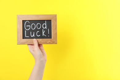 Photo of Woman holding blackboard with words GOOD LUCK on yellow background, closeup. Space for text