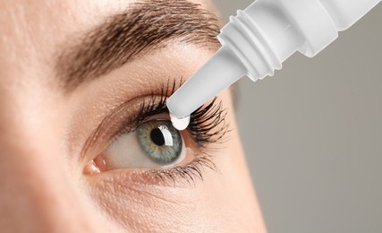 Woman applying eye drops on grey background, closeup