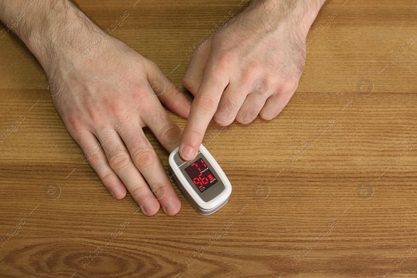Photo of Man using pulse oximeter for oxygen level testing at wooden table, above view