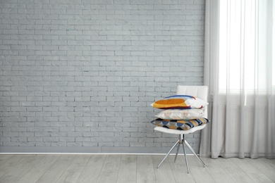 Photo of Different pillows on chair near brick wall in room