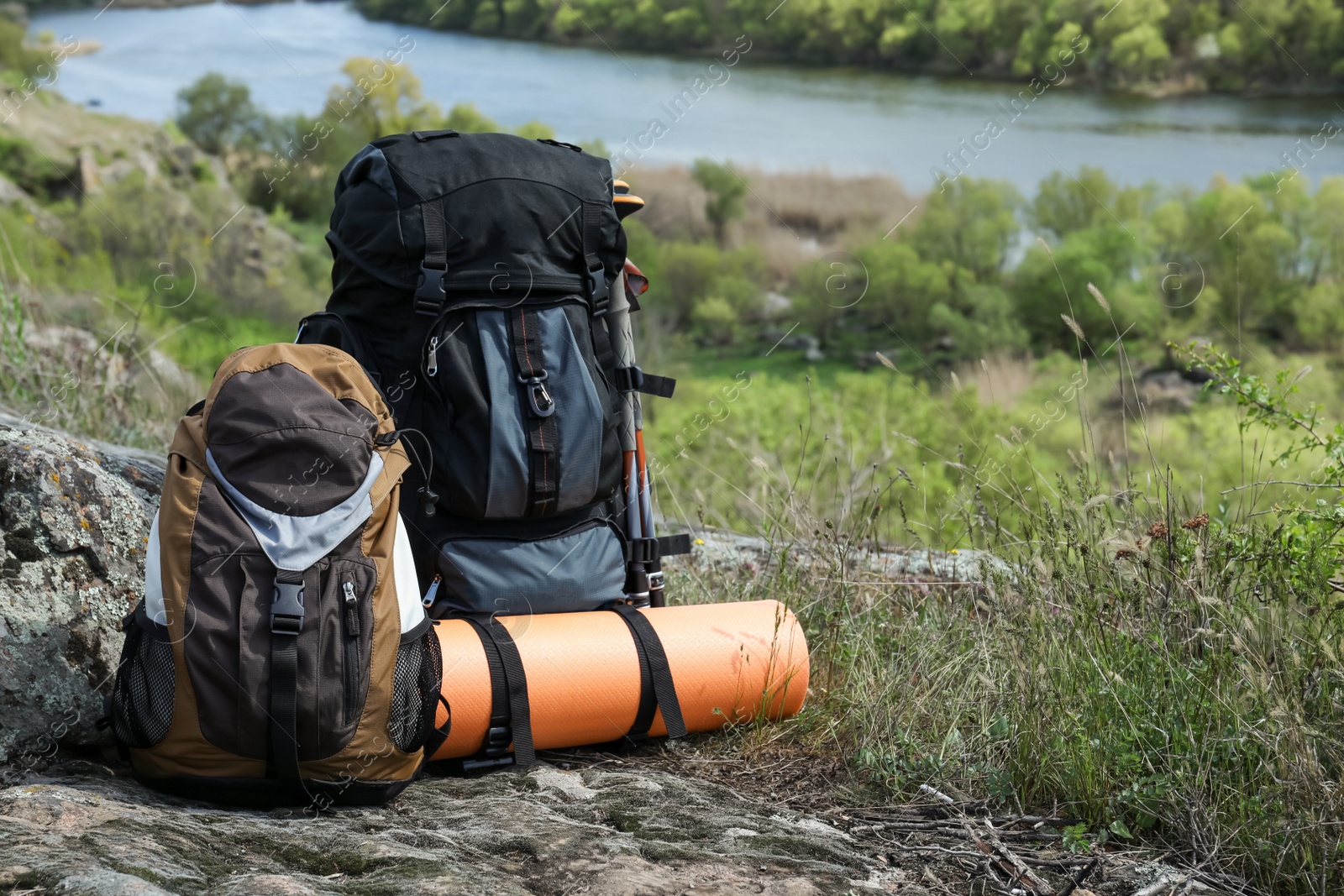 Photo of Backpacks with trekking poles and camping mat on rocky hill, space for text