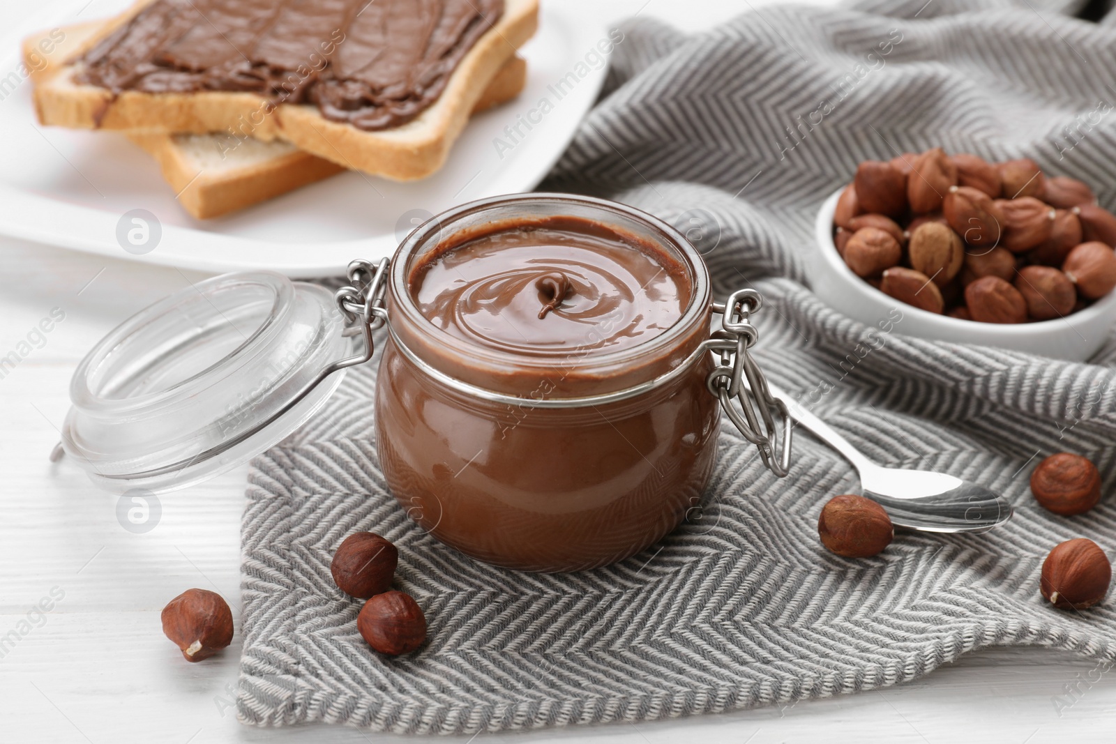 Photo of Jar with chocolate paste, tasty toast and nuts on white wooden table