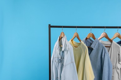 Photo of Rack with stylish clothes on wooden hangers against light blue background, space for text