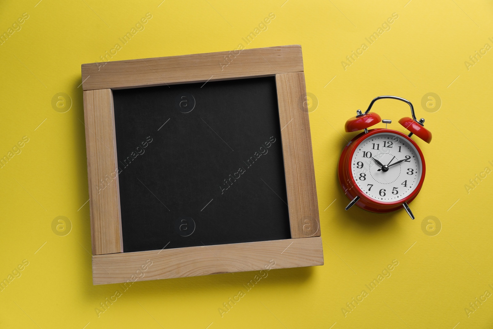 Photo of Blank chalkboard with alarm clock on yellow background, flat lay. Space for text