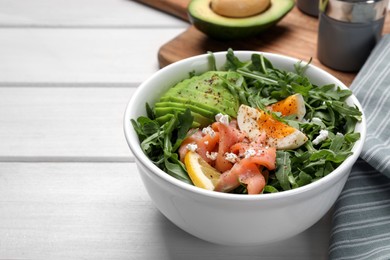 Delicious salad with boiled egg, salmon and avocado in bowl on white wooden table, closeup