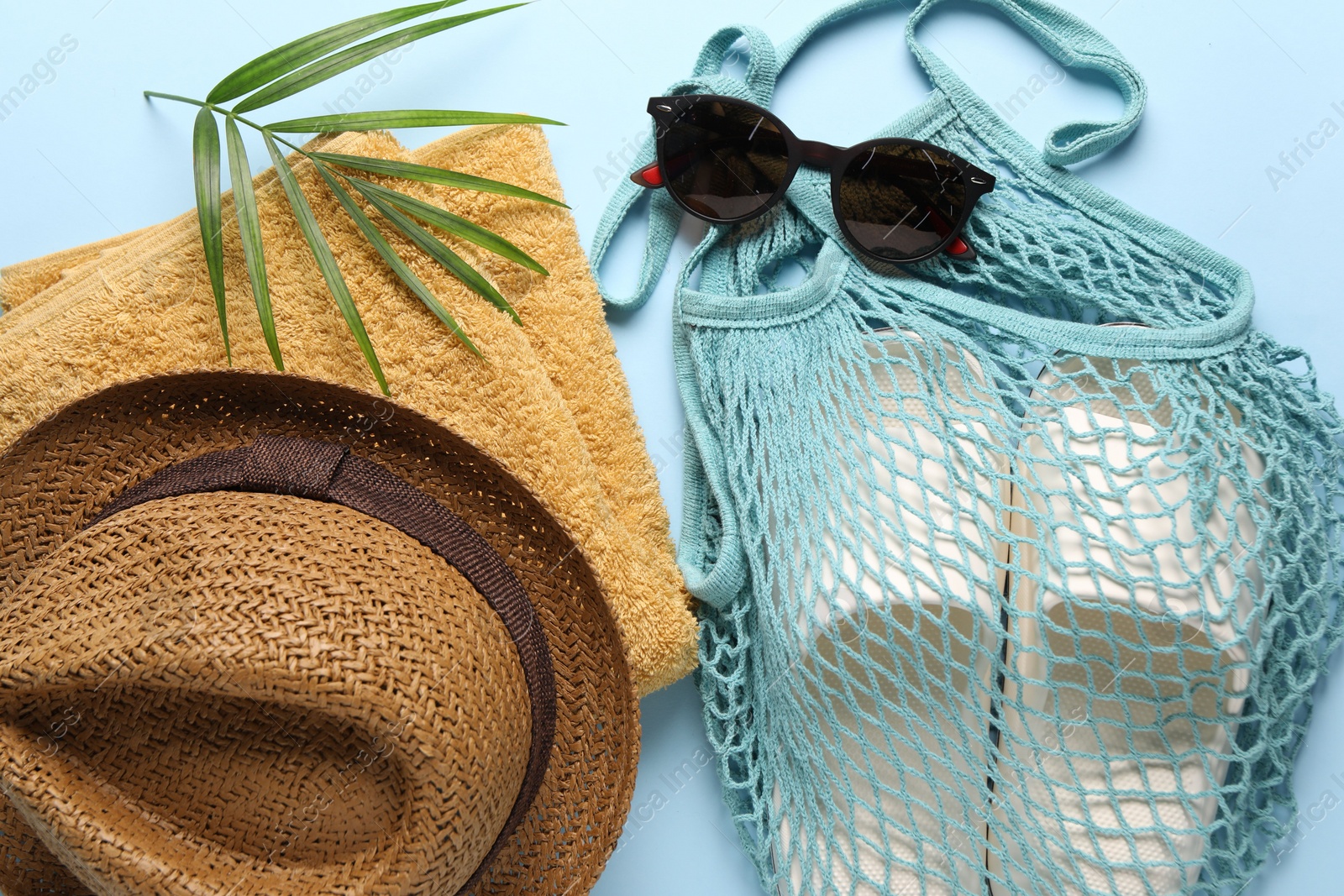 Photo of String bag, different beach accessories and palm leaf on light blue background, flat lay