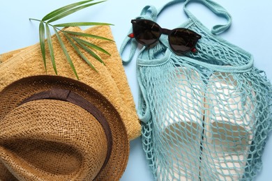 Photo of String bag, different beach accessories and palm leaf on light blue background, flat lay