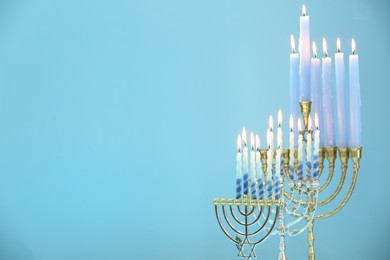 Hanukkah celebration. Menorahs with burning candles on light blue background, space for text