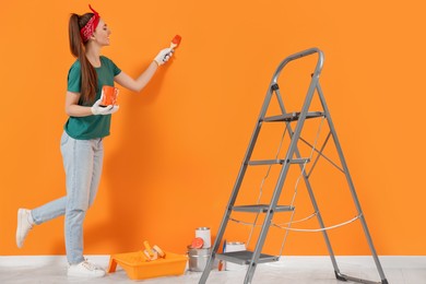 Happy designer painting orange wall with brush indoors
