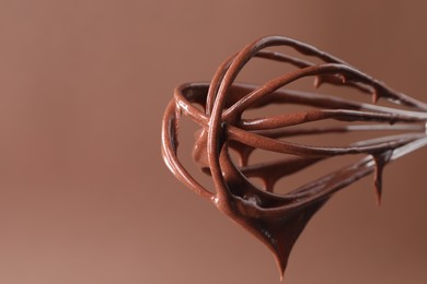Photo of Chocolate cream flowing from whisk on brown background, closeup. Space for text