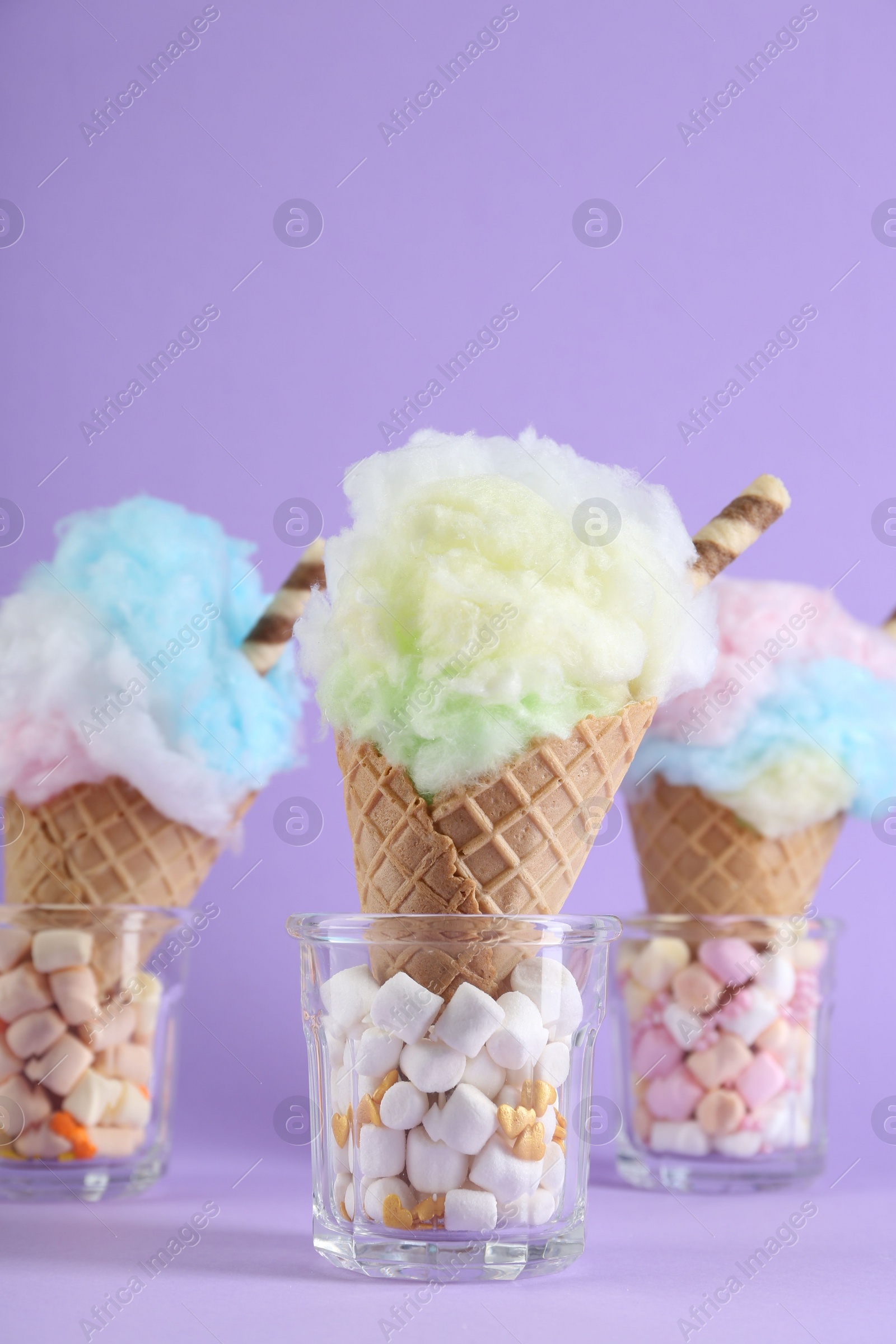 Photo of Sweet cotton candies in waffle cones on purple background