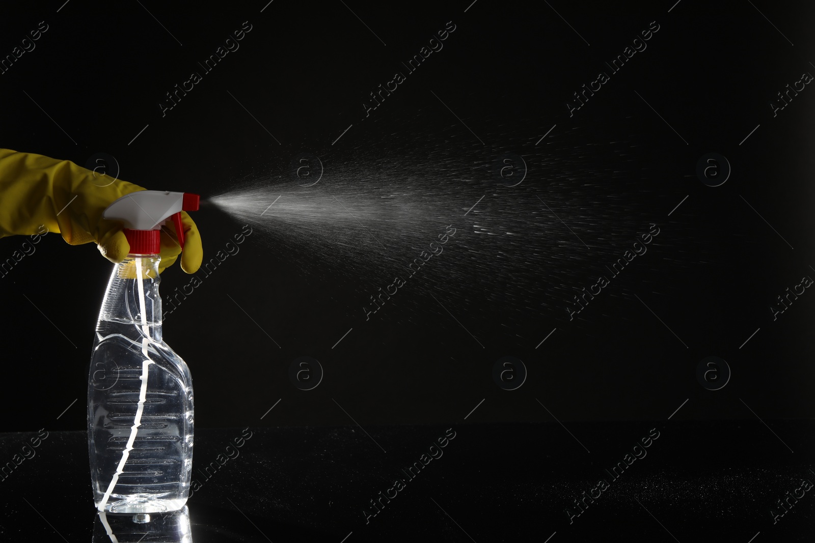 Photo of Woman spraying liquid from bottle on black background, closeup