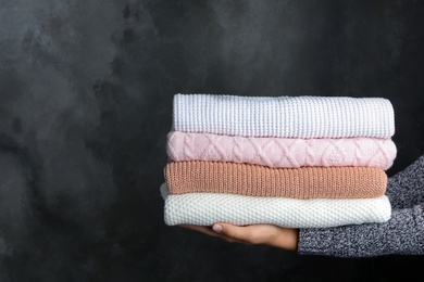 Photo of Woman holding stack of warm clothes on dark background, closeup. Autumn season