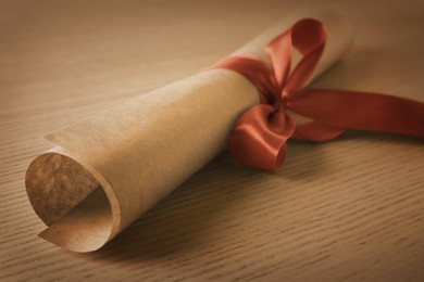 Graduation diploma tied with red ribbon on wooden table, closeup