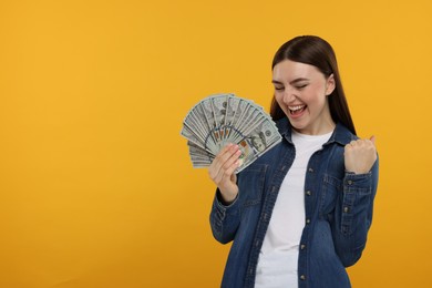 Excited woman with dollar banknotes on orange background, space for text